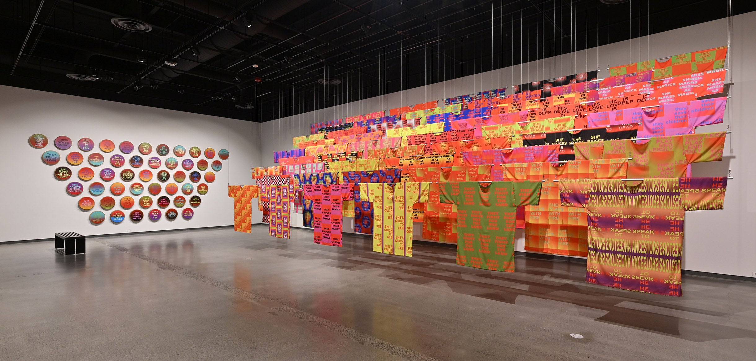 Gallery view of a multicolored installation of textiles including clothing and wall art.
