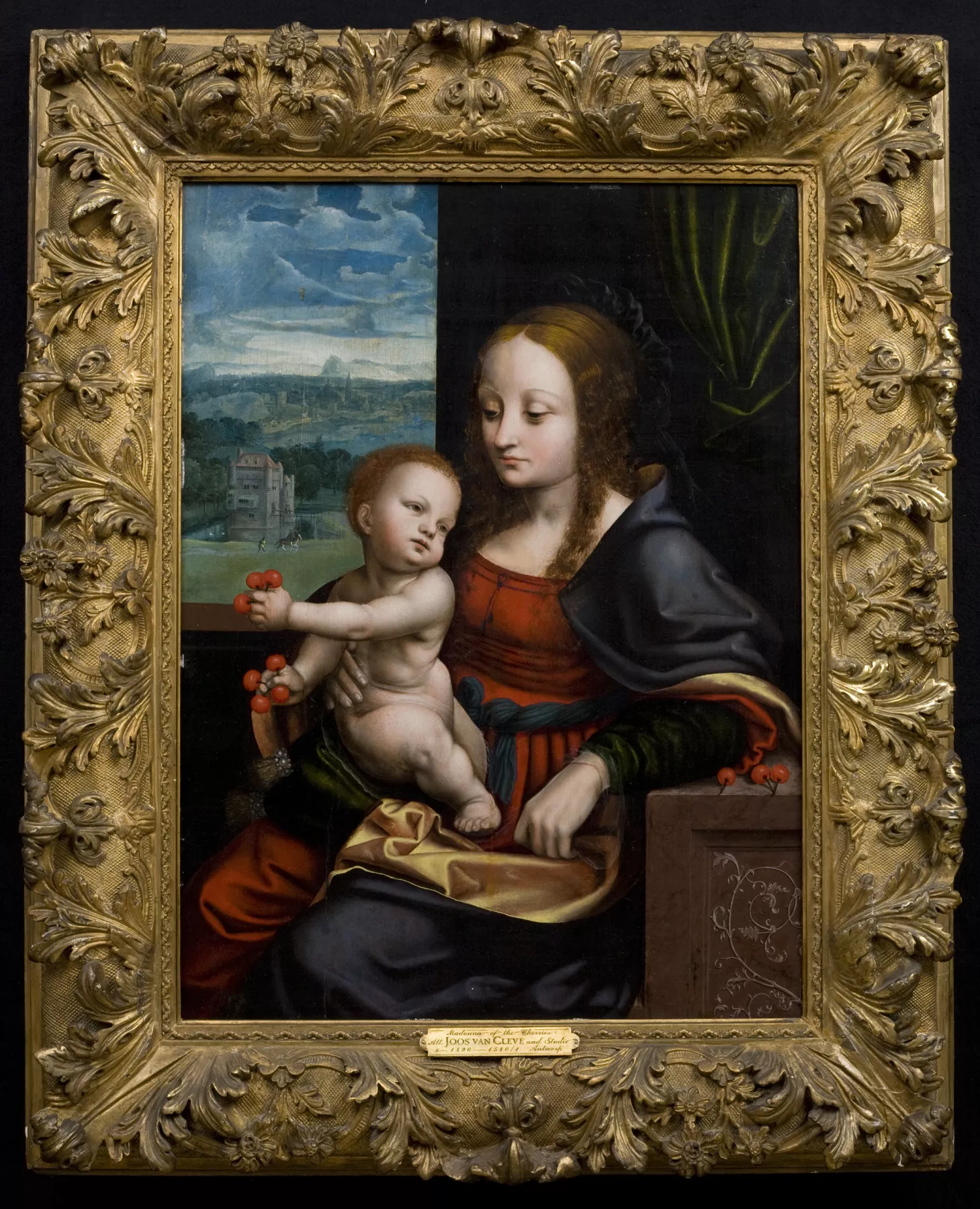 A Renaissance-style painting of the Madonna and Child, where the Madonna is holding the Christ child in her arms while seated, both framed within an ornate gold frame, with a serene landscape visible through a window.