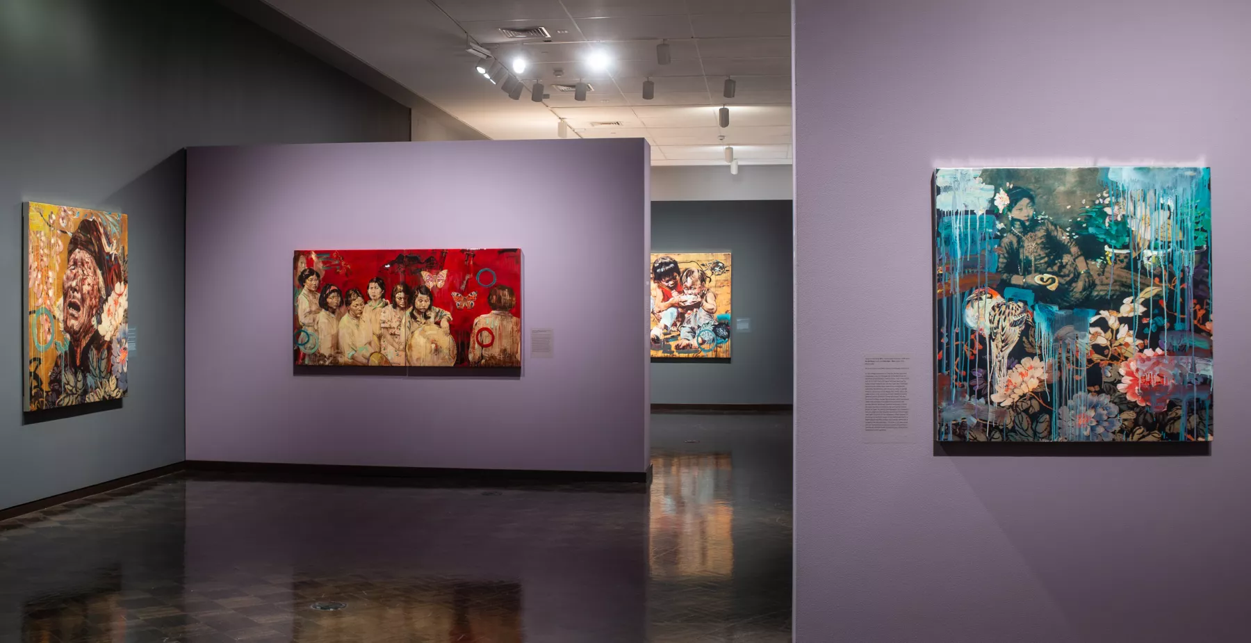 Gallery view showing several paintings of people on the walls. The walls are blue and purple and the dark floor reflects the images.