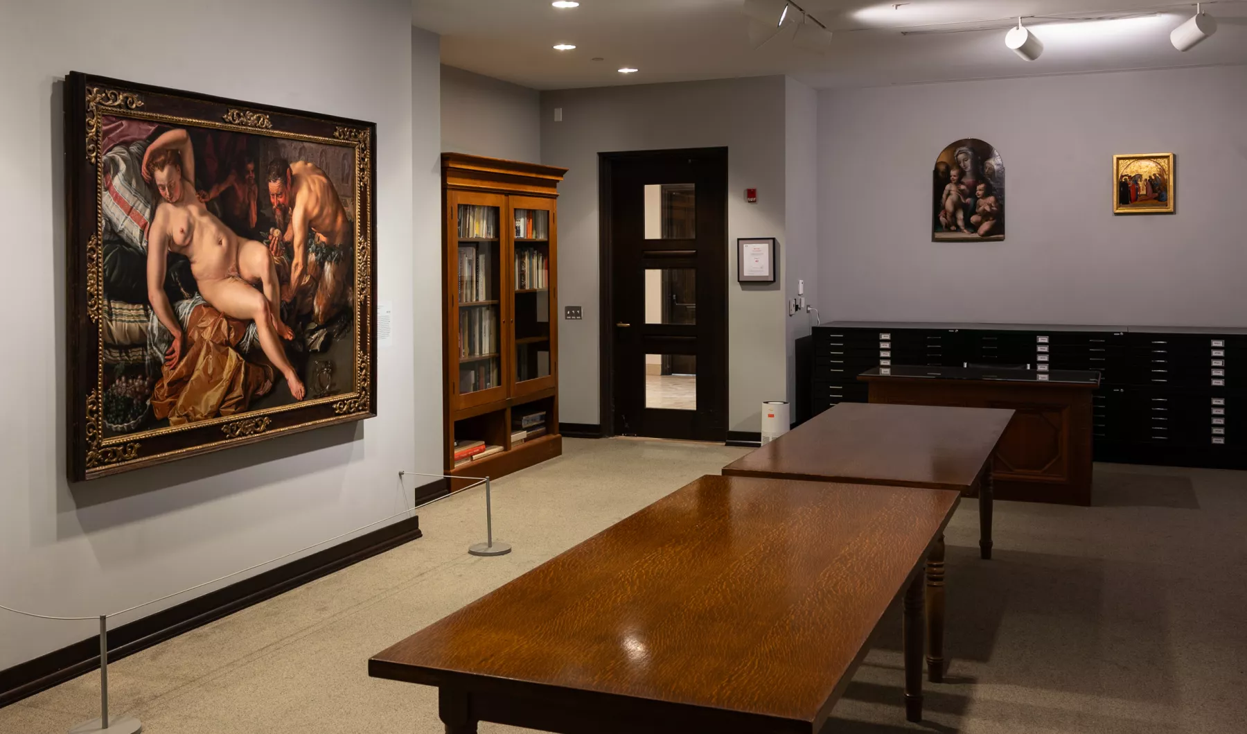 Gilkey Research Center view with several paintings on grey walls and a large wooden table in the middle. Black flat file cabinets line the back wall.
