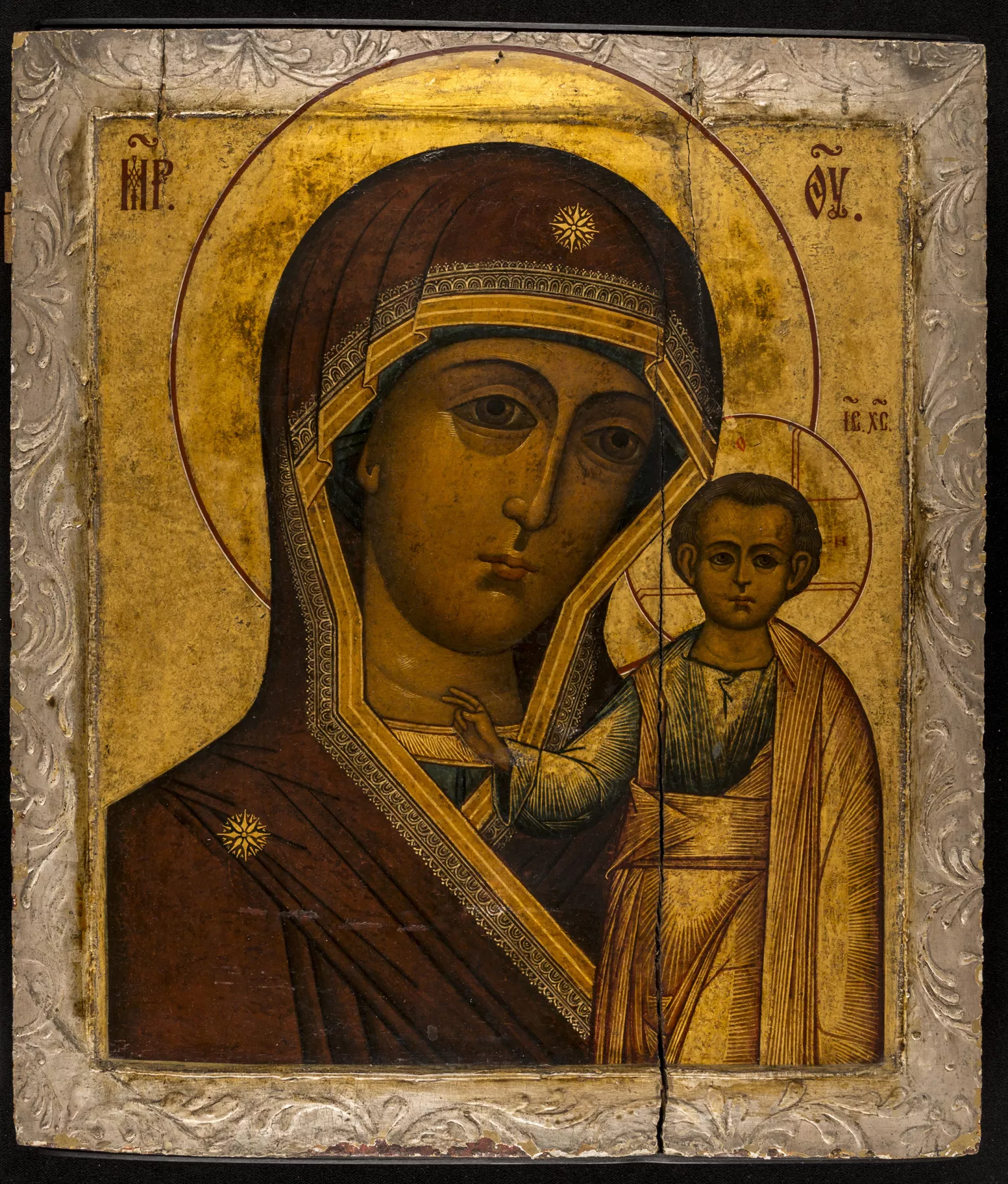 A traditional Russian icon of the Virgin Mary holding the Christ Child, both depicted with solemn expressions and haloed, against a gold-leaf background with intricate patterns.