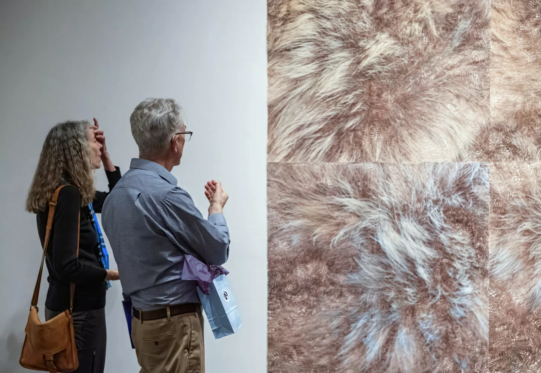 Two people look at art on the wall.