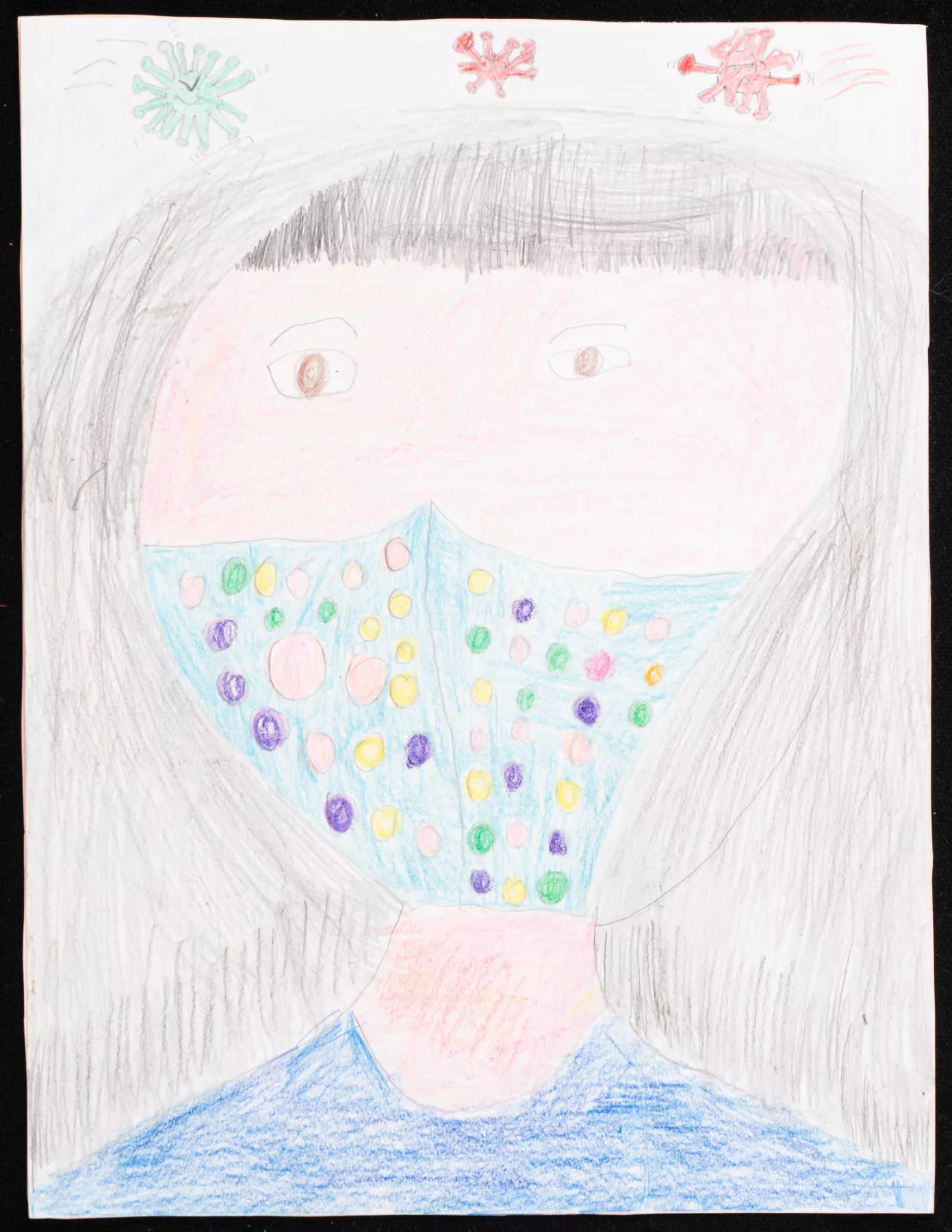 A child's drawing of a person with long black hair wearing a colorful face mask, with two virus illustrations in red and green above their head.