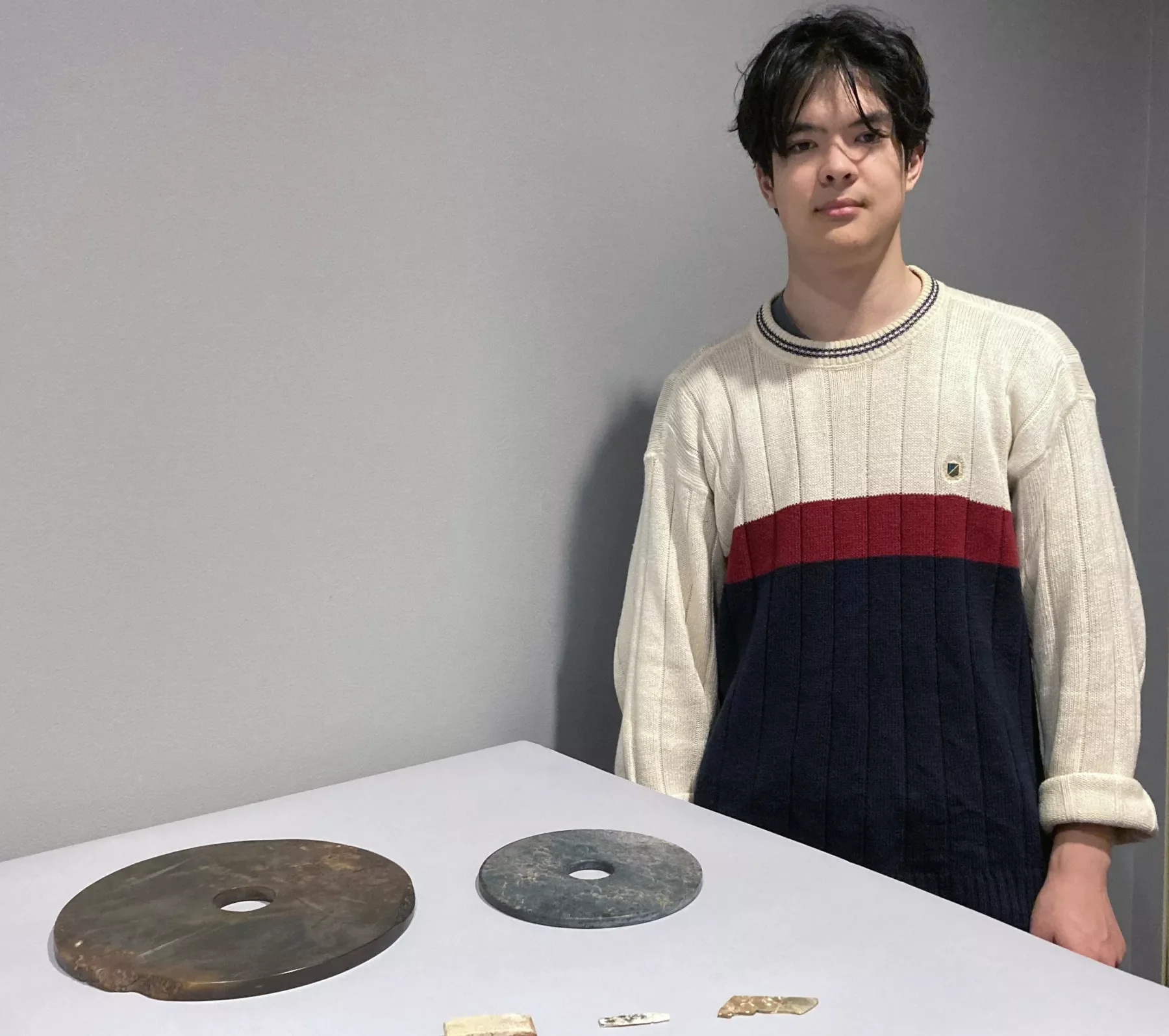 A person standing next to a display of two ancient jade discs and small jade fragments. The discs have central holes and vary in color from brown to greenish-gray.