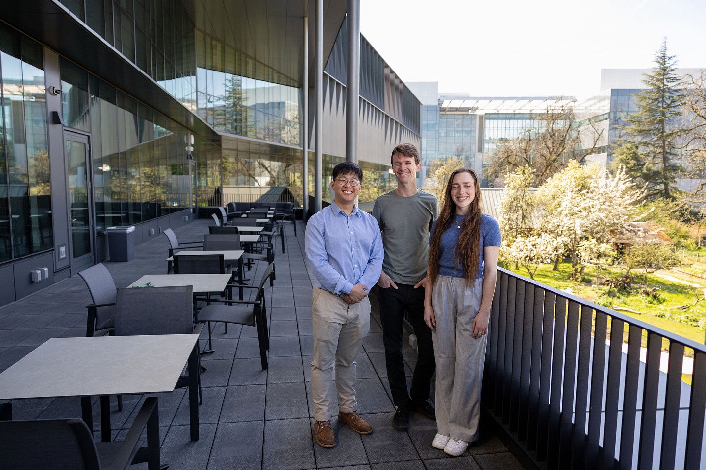 Three people on a terrace, with glass, and knight campus in the background