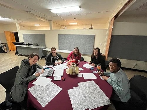 Group of people working around a table with a maroon table cloth