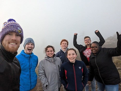 Group of people looking excited because they have completed a hike, which looks foggy in the background