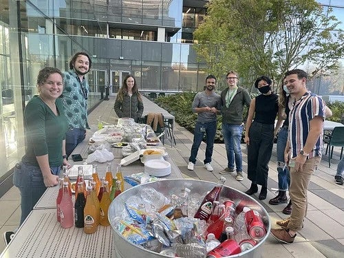 Group of poeple standing around outside, around a table with snacks and drinks