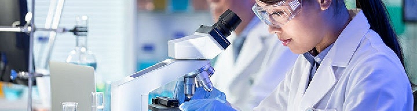 Multiple people wearing white lab coats working on scientific equipment in a lab