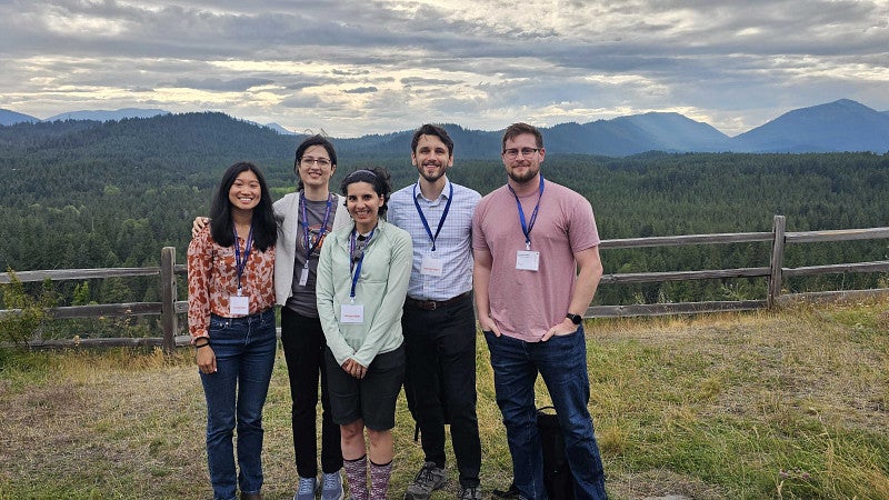 A group of people in front of a mountain scene, with a rugged wooden fence