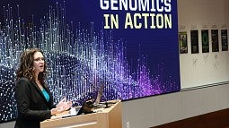 Leslie Coonrod at the podium before a blue graphic for Genomics in Action