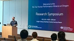 Person at lectern with audience in foreground and slide on screen welcoming people to the Wu Tsai research symposium