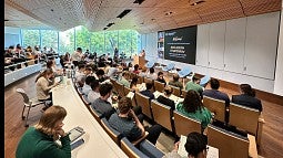 Seminar room with audience in the foreground, speaker at podium in background and slide on screen reading "Inclusion Symposium"