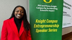 Erika Moore stands to the left of a sign with the words Phil and Penny Knight Campus for Accelerating Scientific Impact