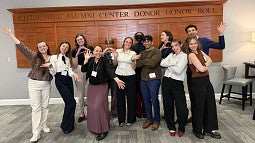 A group of people smiling, wearing business close, posing with their hands up