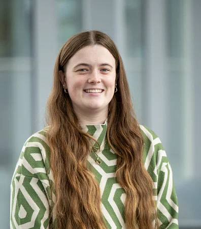 headshot of a woman with long brown hair, in a green and white sweater