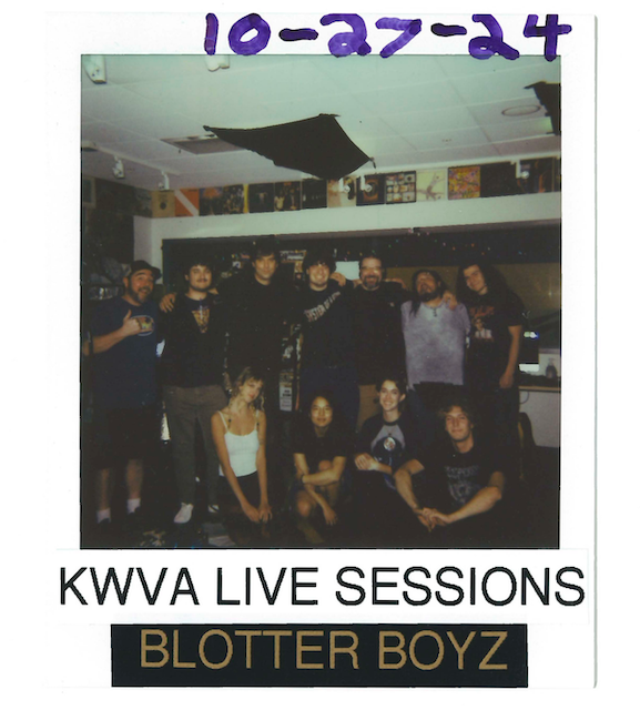 Polaroid framed picture of 11 people, 8 men and 3 women posing for a picture. Seven people are standing behind 3 sitting people. Text above read October 27th 2024, text below read KWVA Live Sessions, Blotter Boys.
