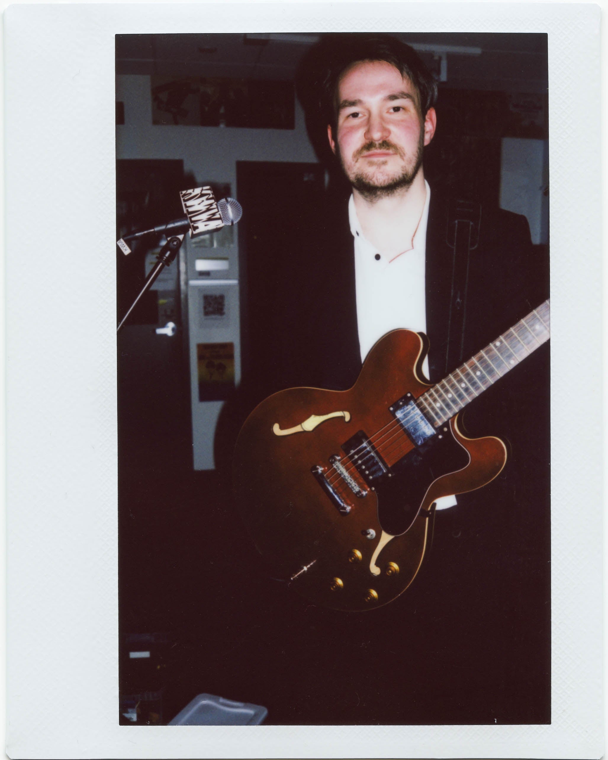 Polaroid picture of the artist known as Candy Cigarettes (white man, tall, short beard) posing in the KWVA studios