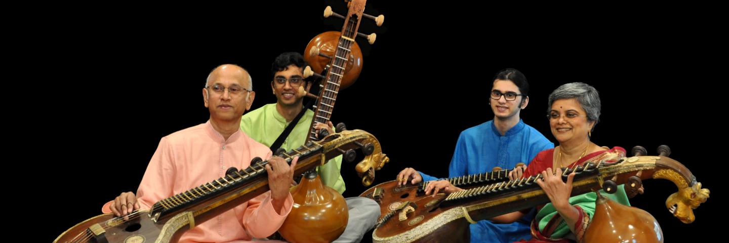 Sreevidhya Chandramouli and three indian men sitting against an all black background. They are all holding veena instruments.