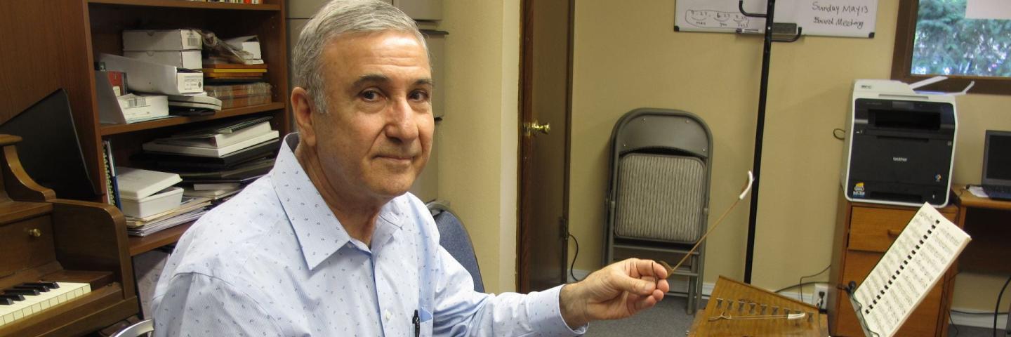 Image of Hossein Salehi playing a santoor, a hammered instrument. Hossein Salehi is a Persian man with gray hair. He is seated in a classroom, wearing a button-down shirt.