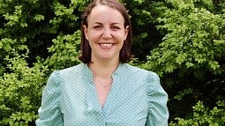 Rebecca Lewis stands in front of an assortment of green bushes. 