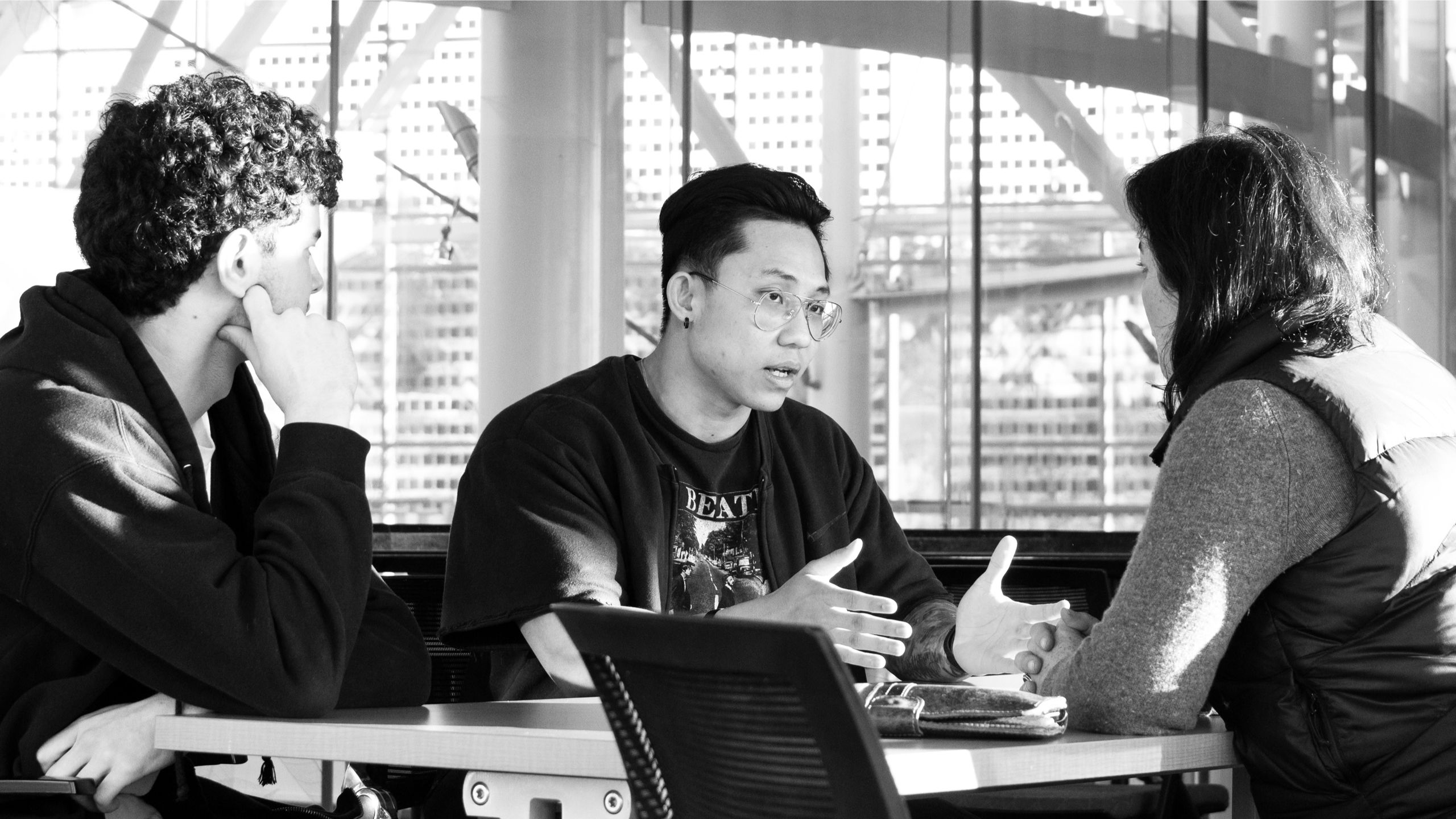 Three students sitting across from each other at a table, talking.