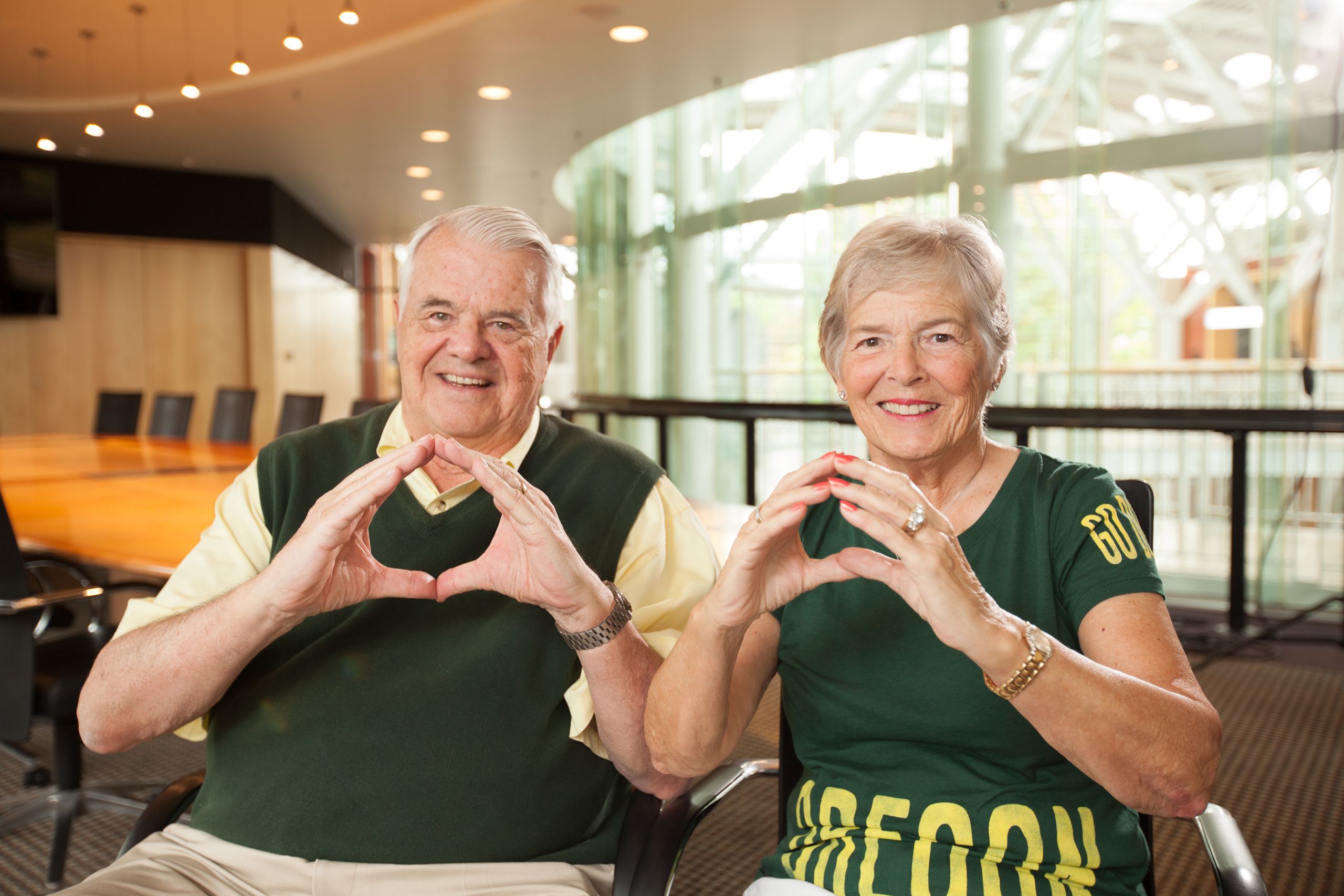 Gerry and Marilyn Cameron sitting and smiling at the camera with their hands in the shape of an O.