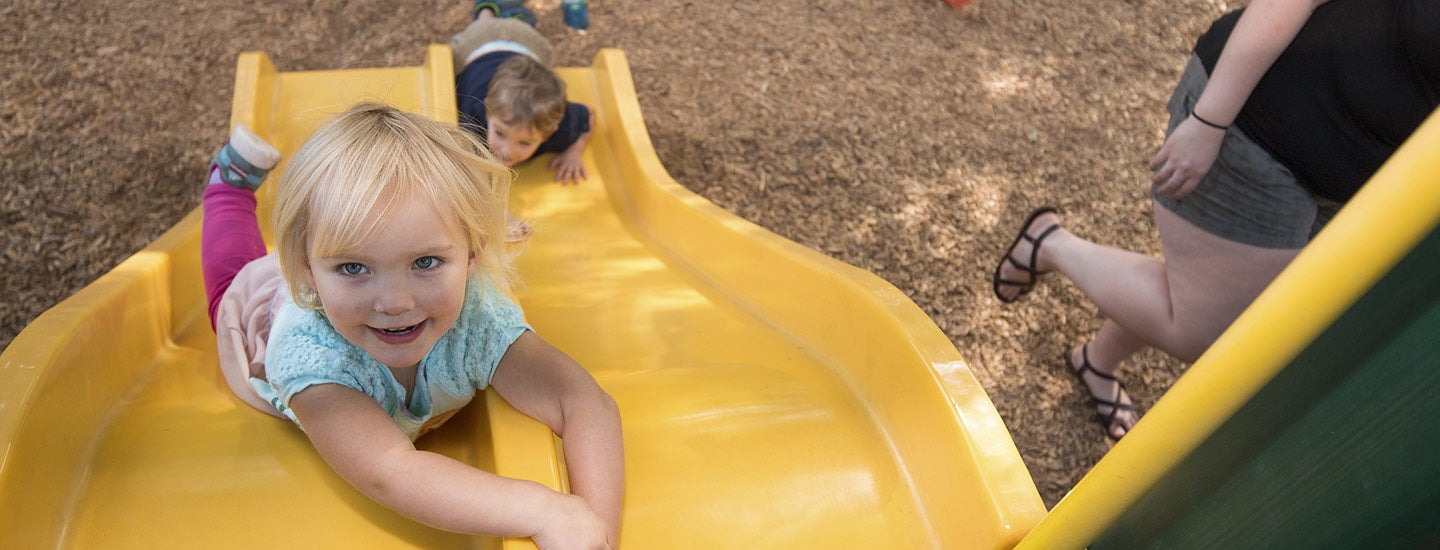 Supervised toddlers playing on slide at Moss Street Children’s playground.