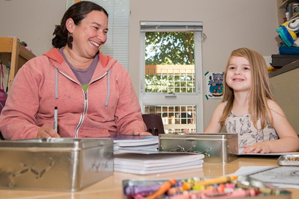 Staff member sitting with child with notebooks and crayons.