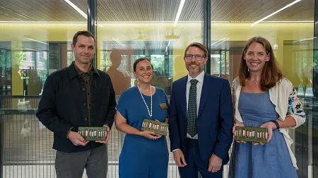 four people posed together, three holding trophies as tiles