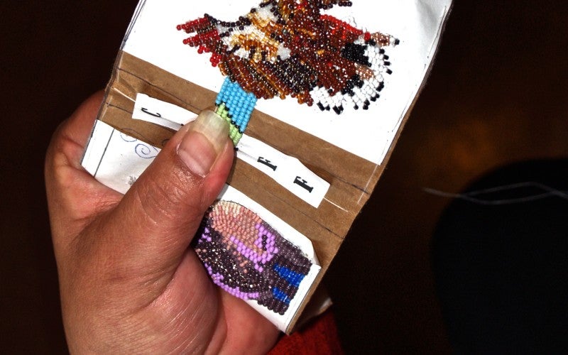 A white piece of cloth with a beaded brown, red, and black bird on it.