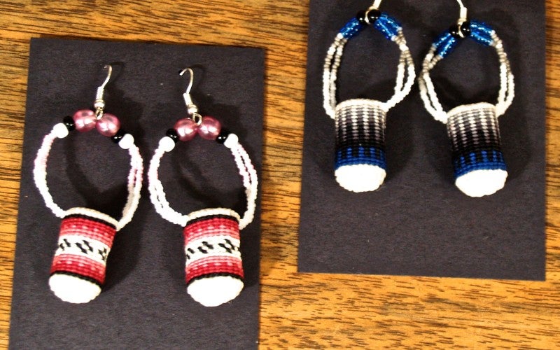 Two pairs of earrings in the shape of miniature baskets. One pair is red, black, and white. The other pair is blue, black, and white.