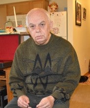 Jamshid sits in a room with a wooden santur instrument. He wears a green sweater with a black abstract pattern on it.