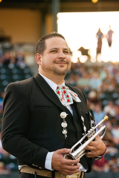 Arturo dressed in mariachi regalia, holding a trumpet.