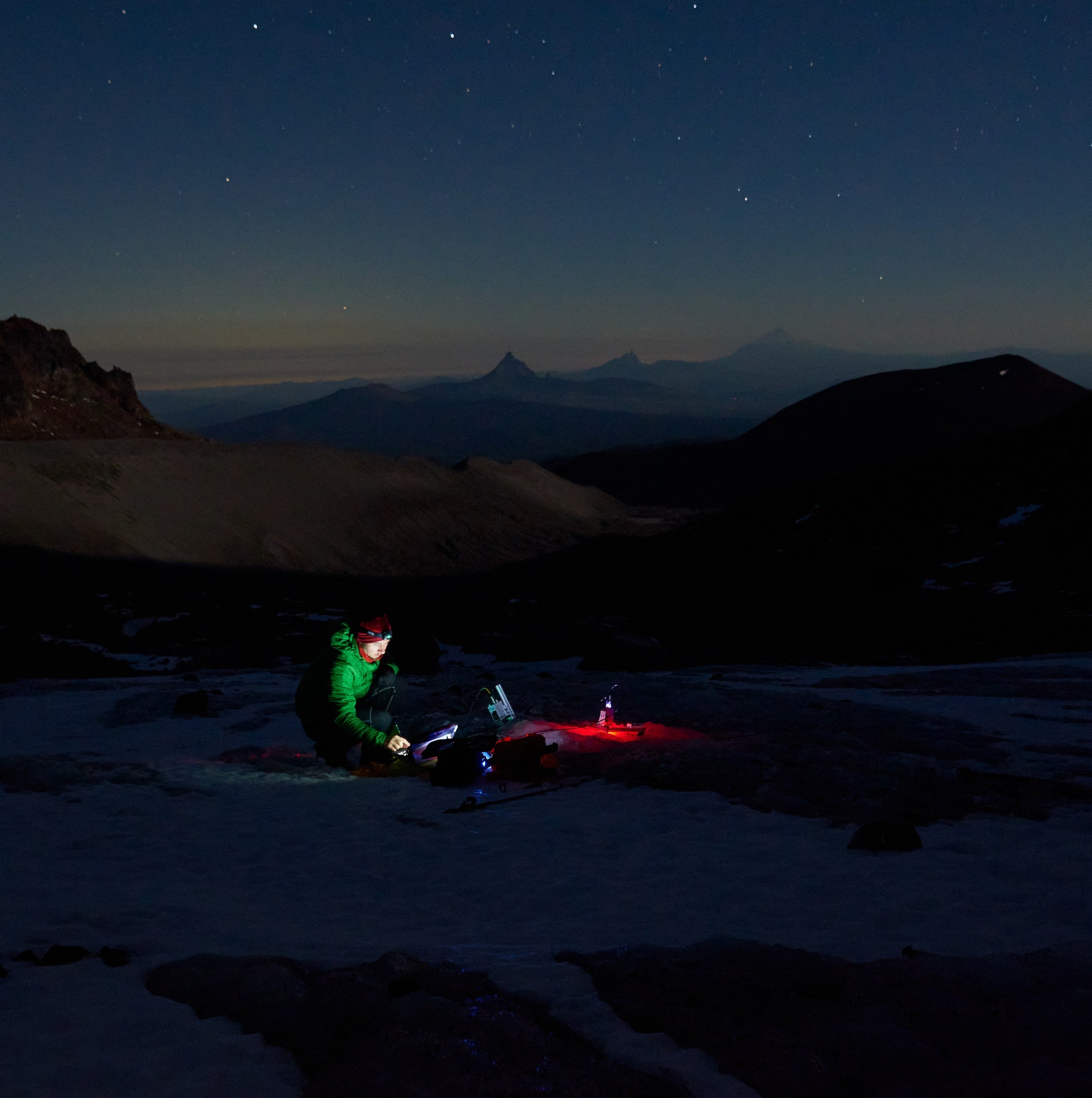 A person crouches to collect measurements from equipment set on the Collier Glacier in the Central Oregon Cascades.