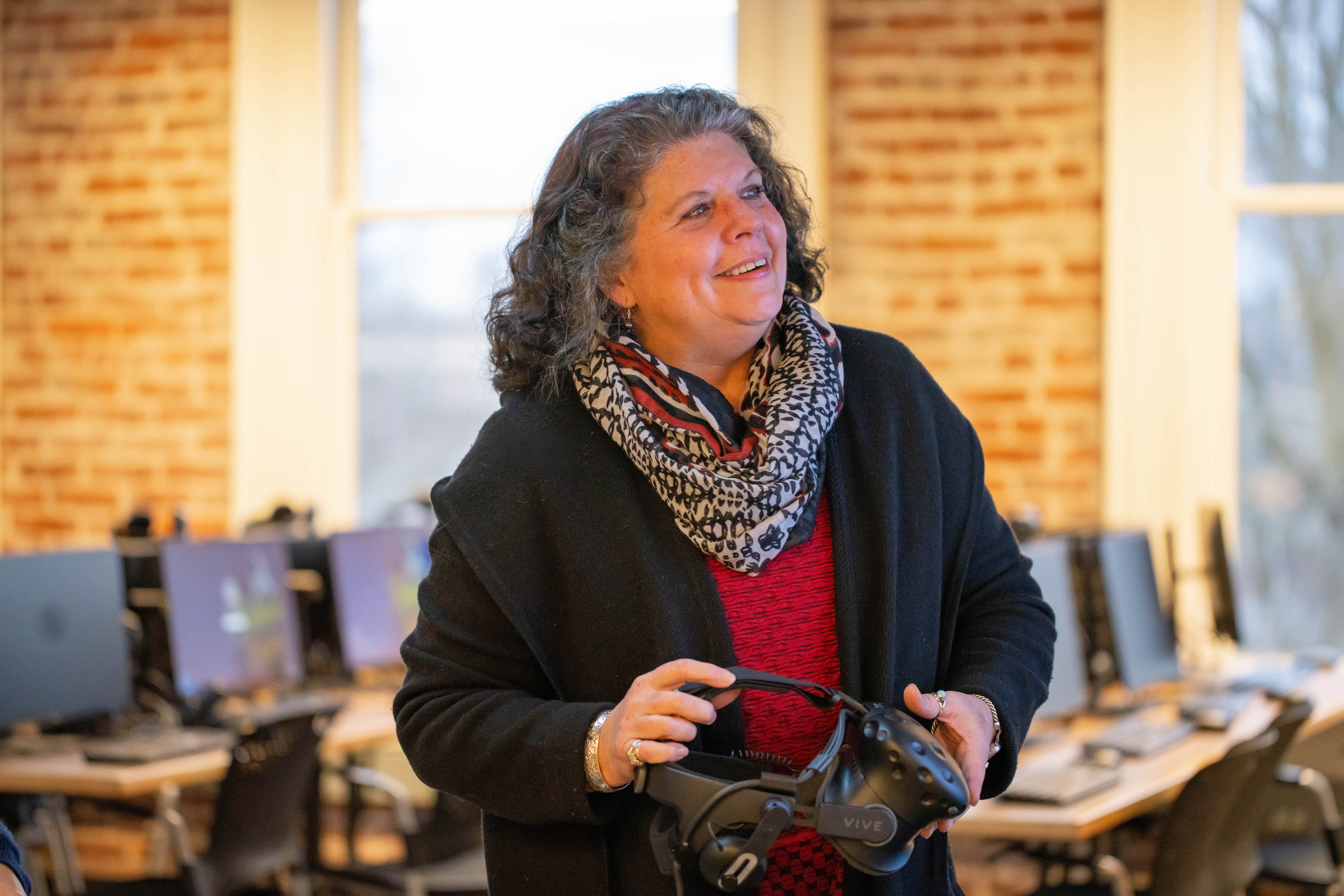 Woman in a computer lab holding a VR set in her hands. 