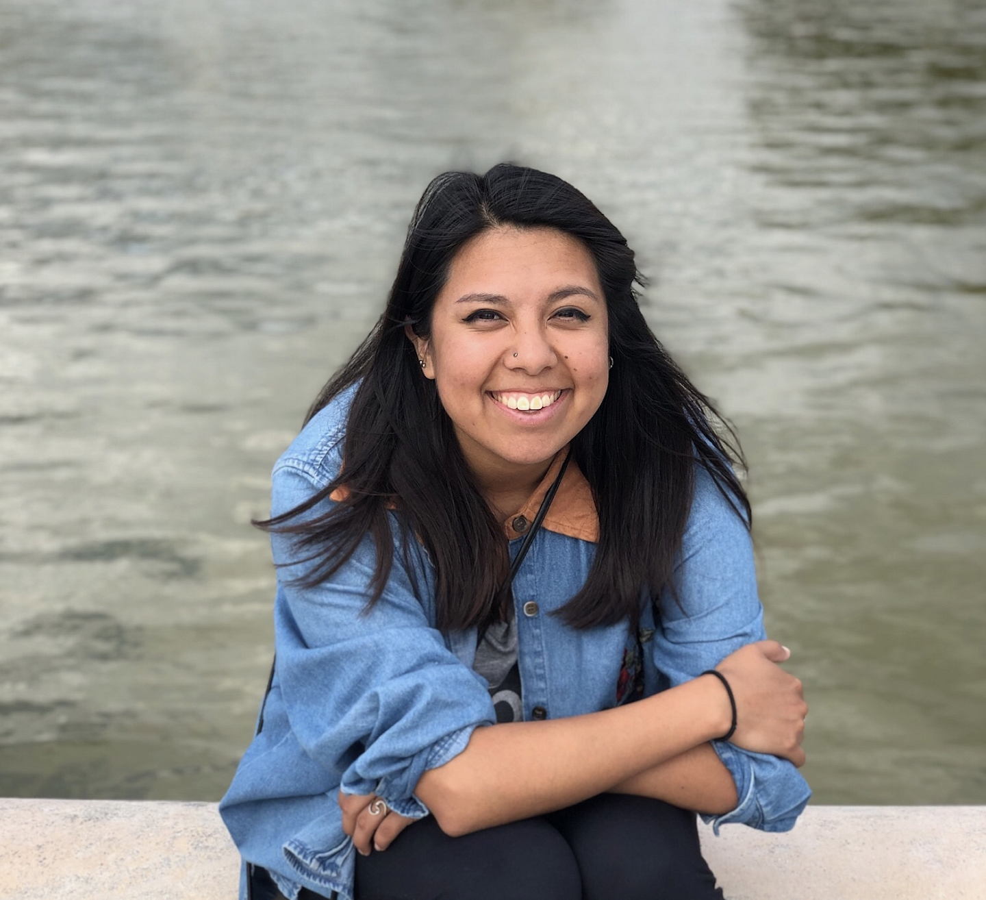 picture of Elizabeth Gillingham sitting in front of a body of water, smiling, with her arms crossed in front of her