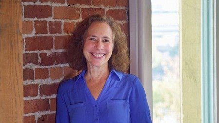 Jane Gordon stands next to a brick wall and a window.
