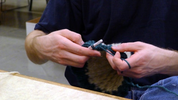 An inmate crochets a scarf at the Oregon State Correctional Institution as part of “Crocheting 4 Community.” The group of about twenty men meet four nights a week to crochet and work in hobby crafts, which they donate to charitable causes. Photo by Ricci Cande. An inmate crochets a scarf at the Oregon State Correctional Institution as part of “Crocheting 4 Community.” The group of about twenty men meet four nights a week to crochet and work in hobby crafts, which they donate to charitable causes. Photo by Ricci Cande.