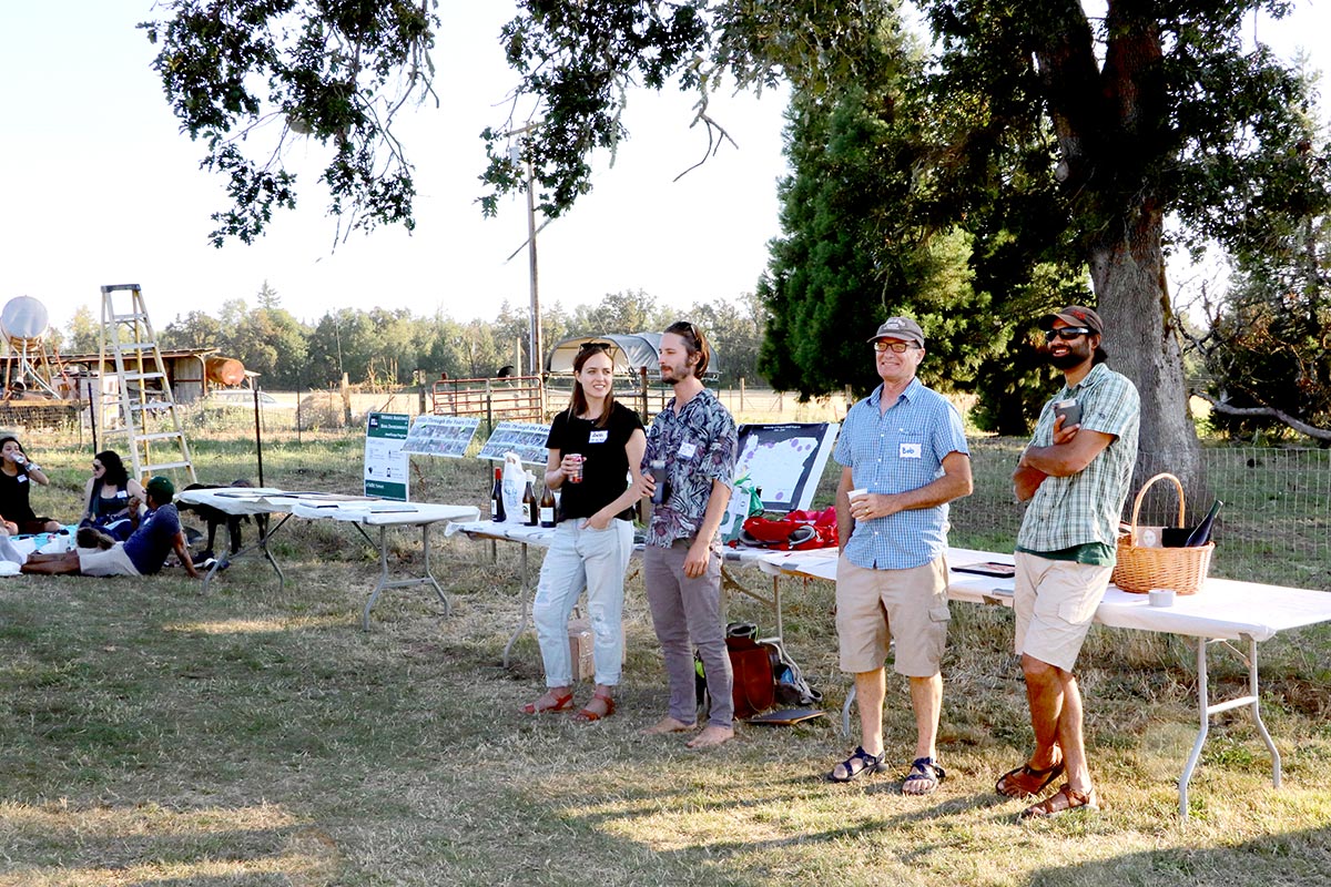 four people standing in front of a table outside in the grass