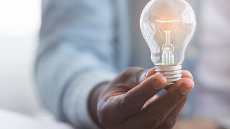 Person wearing a blue sweater with dark skin holding a light bulb