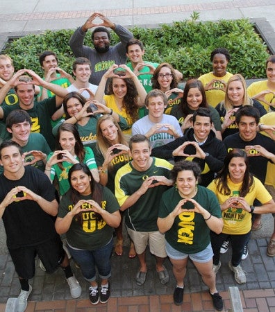 Photo of a dozen students outside on sidewalk, taken from above. Students look up.