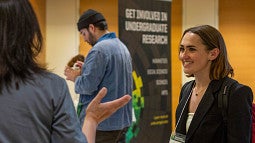 symposium participant talking to person near signage for the event