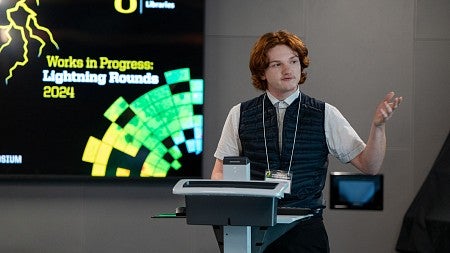 A male student standing at a podium giving a Works in Progress Presentation