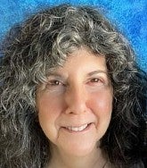 Rachelle (Riki) Saltzman. She has greying curly hair.