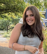 Margaret Grace has long brown hair and a grey shirt.