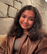 Aishiki Nag has long brown hair and wears a brown leather jacket