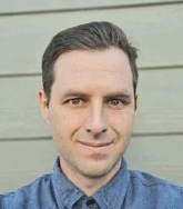 Colin Williamson has short light brown hair and wears a blue shirt