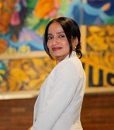 Monica Parra has black hair and wears a white suit