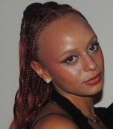 Allinah Williams has braids and a long ponytail and looks at the camera over her shoulder